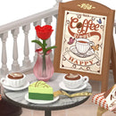 Nahaufnahme des Ladenschilds und des Tisches mit Gebäck, Cappucino und Rose in einer Vase von der Robotime Chic Café Terrace