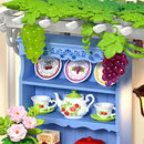 Pergola mit Weinreben und darunter ein blauer Schrank mit ausgestelltem Geschirr im Robotime Midsummer Dream Yard