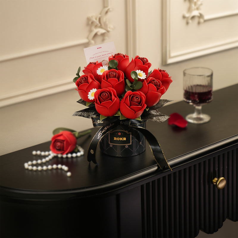 Stilvolle Präsentation des Robotime Red Rose Bouquet, Kunststoff-Bausatz für einen Strauß roter Rosen und weißer Gänseblümchen in einer schwarzen Vase mit schwarzem Band darum